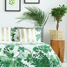 a bed with green leaves on it next to two potted plants and framed pictures