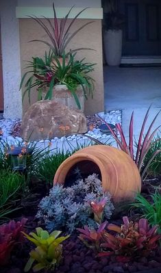 an orange vase sitting in the middle of a garden filled with flowers and plants next to a building