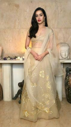 a woman in a white and gold lehenga standing next to a fireplace mantel