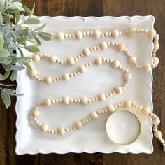 a white tray with beads and a candle on it next to a potted plant