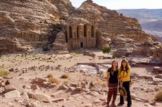 two women are standing in front of some rocks and rock formations at the edge of a canyon