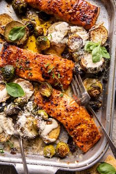 a pan filled with salmon, potatoes and brussels sprouts on top of a table