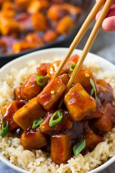 someone is holding chopsticks over rice with tofu and sauce on the side