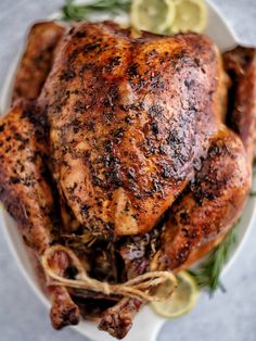 a roasted chicken on a plate with lemons and herbs