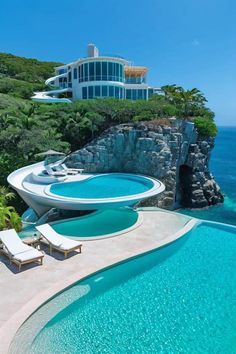 an outdoor swimming pool next to the ocean with chaise lounges and chairs around it