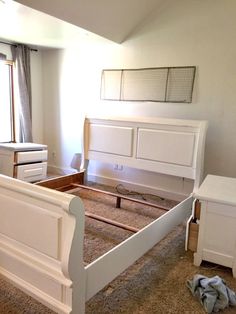 a white bed frame in a bedroom with carpeted flooring and furniture around it