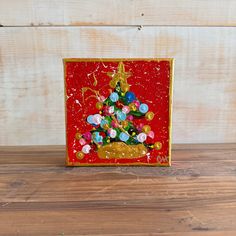 a red and gold christmas card with a tree in the center on a wooden surface