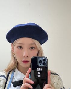 a woman holding up a cell phone in front of her face while wearing a hat