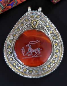 This large Afghan intaglio pendant was handcrafted during the mid-1900's in Central Asia. It is vintage jewelry, not a new reproduction. More measurements are given at the end of the description. Intaglios are designs carved into stone, usually symbolizing something that is culturally significant.  The hand-carved intaglio in the impressive carnelian on this pendant is a prancing gazelle - the spirit animal of grace and agility.  The large tear-drop setting was ornately handmade, with swirls and flourishes in a combination of ornate brass and silver, and a solid back and depth of 1/2 inch. The silver content is 40%. It is in excellent condition, with a warm age-patina (with traces of verdigris) and mild wear-patterns. (Please see images.) To show relative size, I placed it on a new 18-inch Traditional Ceremonial Intaglio Jewelry, Traditional Carved Necklaces For Formal Occasions, Vintage Carnelian Engraved Jewelry, Traditional Oval Ceremonial Necklaces, Traditional Oval Ceremonial Necklace, Traditional Oval Necklaces For Ceremonial Occasions, Ornate Intaglio Necklace As Gift, Traditional Amber Jewelry With Carved Details, Antique Carved Carnelian Jewelry