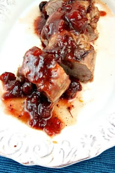 two pieces of meat covered in sauce on top of a white plate with blue cloth