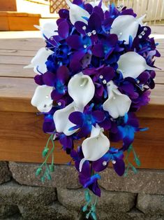 a bridal bouquet with blue and white flowers on it's side, sitting in front of a brick wall