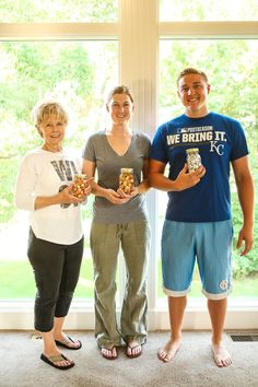 three people standing next to each other in front of a window holding small objects and smiling at the camera