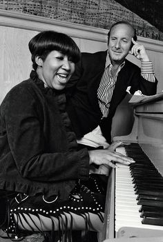 a man and woman are sitting at a piano smiling while talking on their cell phones