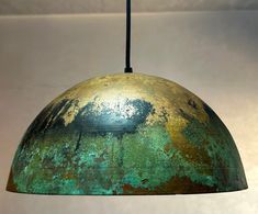 a green and gold colored metal light hanging from a ceiling fixture in a white room