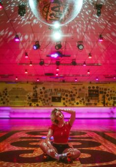 a woman sitting on the floor in front of a disco ball with her hands behind her head