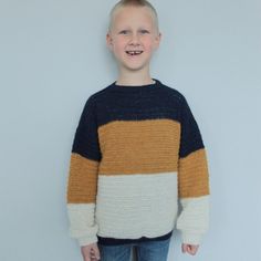 a young boy standing in front of a white wall wearing a sweater with two colors