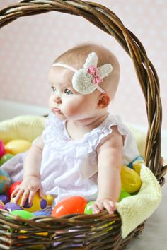 a baby sitting in a basket with an easter egg on the floor next to it