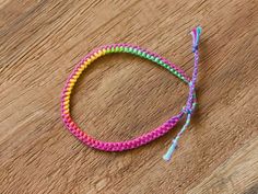 a close up of a colorful bracelet on a wooden surface with a string attached to it