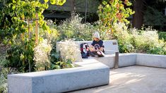 a man sitting on a cement bench in a garden with trees and plants around him