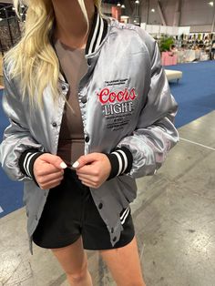 A statement piece! The Coors Light Bomber Jacket. We all may not be as good of an athlete as Patrick, but we can dress like him! Such a killer piece and a limited edition, has a looser fit. Model is wearing a small. Featuring Silver Satin with cotton flannel fill and silk taffeta printed lining. Matte black snap front closure with welt hand pockets at front. Stripe rib collar, cuffs and hem. Embroidered official collaboration logo on chest and back. A sponsored look, without the contract- this u Collaboration Logo, Silk Taffeta, Coors Light, Ribbed Neckline, Cotton Flannel, American Girl, Varsity Jacket, Matte Black, Bomber Jacket