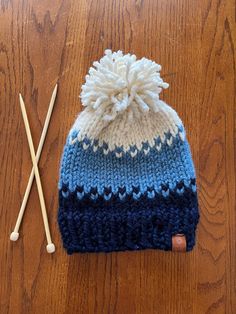 two knitting needles and a knitted hat on a wooden surface