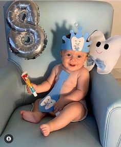 a baby sitting on a blue chair wearing a crown and holding a toothbrush in his hand