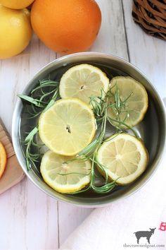 lemons and rosemary in a bowl next to oranges