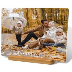 a family sitting on the ground with an umbrella in their hands and leaves around them