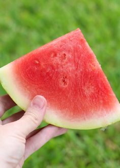 a piece of watermelon being held by someone's hand in the grass