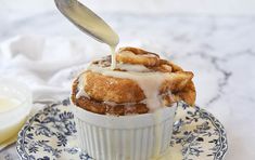 a cinnamon roll being drizzled with icing on a blue and white plate