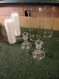 four glass vases sitting on top of a counter next to a bottle and two glasses