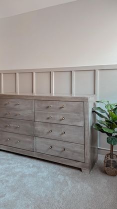 a bedroom with a large gray dresser next to a potted plant on the floor