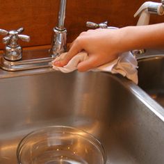 a person cleaning a stainless steel sink with a cloth on it's side and a hand holding a rag