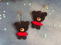 two black teddy bears with red scarves hanging from earwires on a gray surface