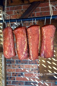 three raw meats hanging from a line in front of a brick wall with sunlight streaming through them