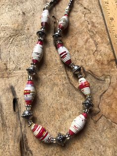 a red and white beaded necklace sitting on top of a wooden table next to a ruler