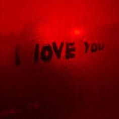 the word i love you is written in black ink on a red background with an orange light behind it