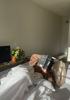 an unmade bed with two books on top of it and a television in the background