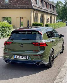 the rear end of a green volkswagen suv driving down a street in front of a house