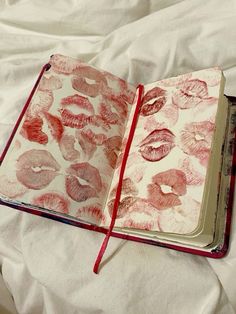 an open notebook with lipstick drawn on it sitting on top of a white bed sheet