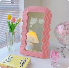 a pink mirror sitting on top of a table next to a vase with tulips