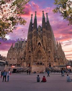 people sitting on the ground in front of a tall building with spires and flowers