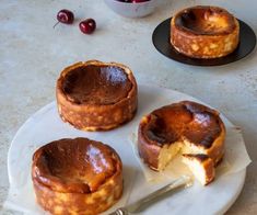 three baked desserts on a plate with a knife and bowl of cherries in the background