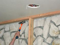 a man holding a hammer in front of a rock wall with a hole in the ceiling