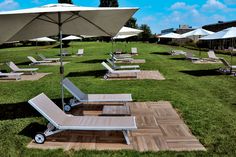 lounge chairs and umbrellas are set up on the grass in front of an open field