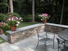 an outdoor patio with potted flowers on the wall and table in the middle, surrounded by trees