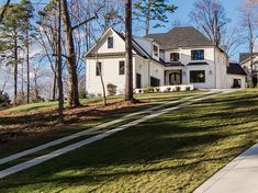 a large white house sitting on the side of a lush green field next to trees