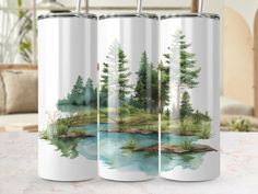 three travel mugs sitting on top of a table next to each other with water and trees painted on them