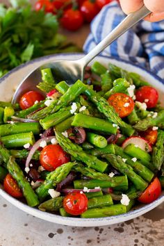 a bowl filled with asparagus, tomatoes and other veggies on top of a table