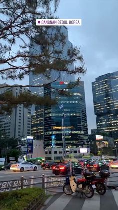 two motorcycles are parked in front of some tall buildings at night with cars passing by